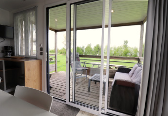 Uitzicht vanuit de woonkamer op het overdekte terras met bank en tafel in Terrace Lodge 2, Nederland.