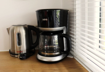 Elektrische waterkoker en koffiemachine op het aanrecht naast het raam met jaloezieën in een chaletkeuken.
