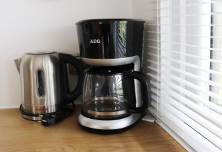 Bollitore elettrico e macchina del caffè su un ripiano vicino a una finestra con veneziana in un chalet.