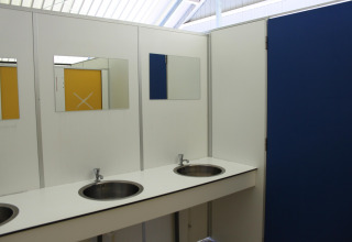 Innenansicht eines öffentlichen Badezimmers mit zwei Waschbecken, Spiegeln und blauen sowie gelben Türen.