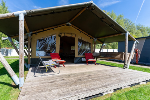 Safari-Zelt 'Heeg' in den Niederlanden mit Holzterrasse, Gartenmöbeln und grünem Rasen im Freien.