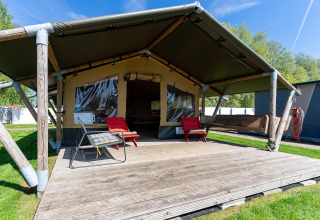Safari-Zelt 'Heeg' in den Niederlanden mit Holzterrasse, Gartenmöbeln und grünem Rasen im Freien.