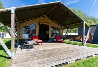 Safari-telt 'Heeg' i Holland med træterrasse, havemøbler og grønne omgivelser under blå himmel.