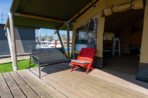 Holzterrasse mit Sitzbank und rotem Stuhl vor einem Safarizelt am Yachthafen in den Niederlanden.