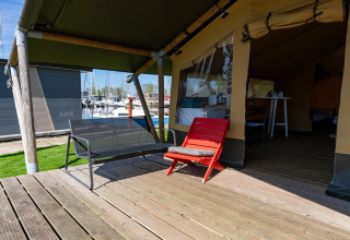 Holzterrasse mit Sitzbank und rotem Stuhl vor einem Safarizelt am Yachthafen in den Niederlanden.