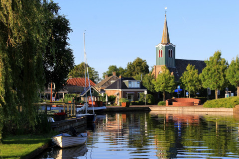 Idyllischer Kanal in Heeg, Niederlande, mit Booten, Kirche, Bäumen und charmanten Häusern.