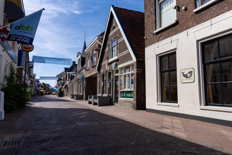 Straßenszene in Heeg, Niederlande, mit traditionellen Häusern, Geschäften und einem klaren Himmel.
