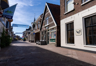 Straßenszene in Heeg, Niederlande, mit traditionellen Häusern, Geschäften und einem klaren Himmel.