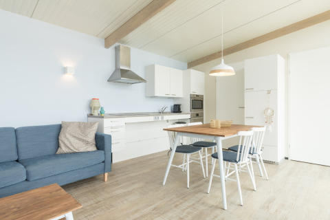 Lichte, modern ingerichte woonkeuken in Sea Lodges Ameland 4 met eettafel, zetel en Scandinavische stijl.