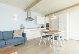 Lichte, modern ingerichte woonkeuken in Sea Lodges Ameland 4 met eettafel, zetel en Scandinavische stijl.