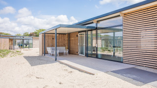 Modern strandhuis Sea Lodges Ameland 4 met houten terras, zitruimte buiten en zandrijke omgeving.