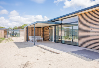 Casa de playa moderna Sea Lodges Ameland 4 con terraza de madera y asientos rodeados de arena.