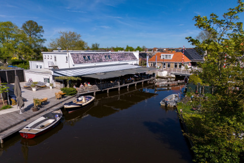 Safari-Zelt in Heeg, Niederlande, an einem Kanal mit Booten, Terrasse und grünem Umfeld bei Sonnenschein.