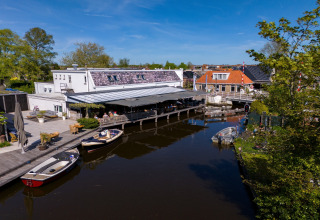 Safari-Zelt in Heeg, Niederlande, an einem Kanal mit Booten, Terrasse und grünem Umfeld bei Sonnenschein.