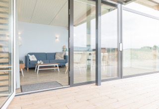 Lichte zithoek in Sea Lodges Ameland 4 strandhuis, met sofa, tafel en grote glazen deur naar het terras.