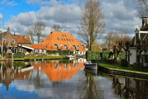 Blick vom Safari-Zelt auf einen Kanal mit Boot und orangegedeckten Häusern in Heeg, Niederlande.