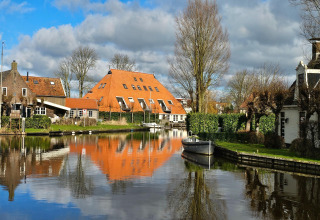 Blick vom Safari-Zelt auf einen Kanal mit Boot und orangegedeckten Häusern in Heeg, Niederlande.