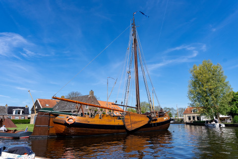 Traditionelles Segelboot liegt am Ufer nahe Safari Tent Heeg, mit Häusern im Hintergrund und blauem Himmel.