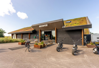 Afbeelding van de receptie van een strandhuis met groendak, fietsen en e-scooters buiten.