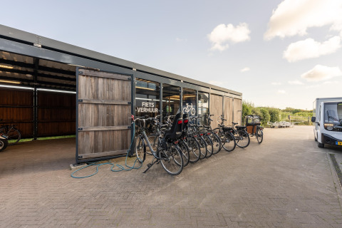 Fietsverhuur bij een strandhuis met meerdere fietsen geparkeerd voor een schuur op een zonnige dag.