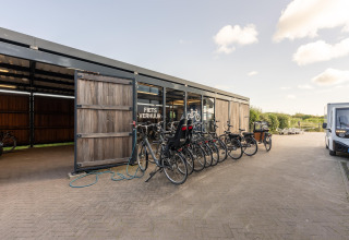 Fietsverhuur bij een strandhuis met meerdere fietsen geparkeerd voor een schuur op een zonnige dag.