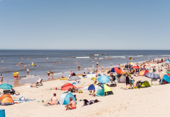 Día concurrido en la playa frente a Sea Lodges «Ameland 4» en los Países Bajos con gente y sombrillas.