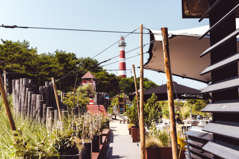 Wandelpad bij een strandhuis met planten, buitenzitjes en achteraan een rood-witte vuurtoren.