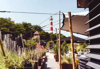 Wandelpad bij een strandhuis met planten, buitenzitjes en achteraan een rood-witte vuurtoren.