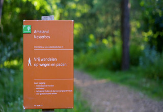 Informatiebord aan de ingang van Nesserbos, Ameland, met groen en een wandelpad op de achtergrond.