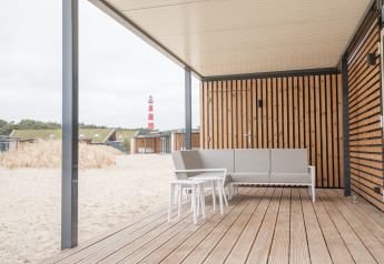 Strandterrasse mit modernen Möbeln und Blick auf einen Leuchtturm bei Sea Lodges Ameland in den Niederlanden.