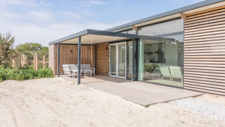 Modern strandhuis Sea Lodges Ameland 3 met houten terras, grote ramen en omringd door zand.