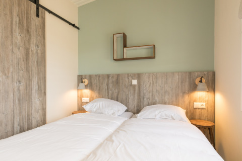Lichte kamer met twee aparte bedden, houten hoofdbord en minimalistische deco in Sea Lodges Ameland 3.