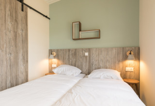 Lichte kamer met twee aparte bedden, houten hoofdbord en minimalistische deco in Sea Lodges Ameland 3.