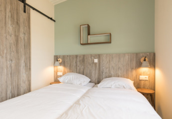 Modernes Schlafzimmer mit zwei Einzelbetten, Holzpaneelen und stilvollen Wandlampen in den Sea Lodges Ameland 3.