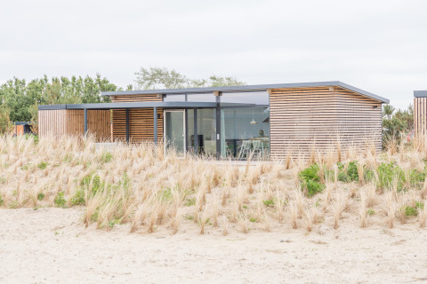 Modern strandhuis met grote ramen en houten panelen, omgeven door duinen bij Sea Lodges Ameland.