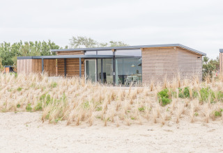 Modern strandhuis met grote ramen en houten panelen, omgeven door duinen bij Sea Lodges Ameland.