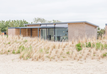 Modernes Strandhaus mit großen Fenstern und Holzverkleidung, umgeben von Dünen bei Sea Lodges Ameland.