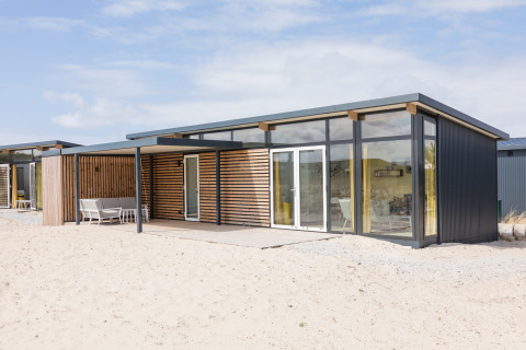 Moderne strandlodge bij Sea Lodges Ameland 2, met grote glazen ramen en houten details op het zand.