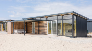 Moderne strandlodge bij Sea Lodges Ameland 2, met grote glazen ramen en houten details op het zand.