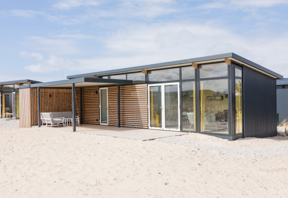 Moderne strandlodge bij Sea Lodges Ameland 2, met grote glazen ramen en houten details op het zand.