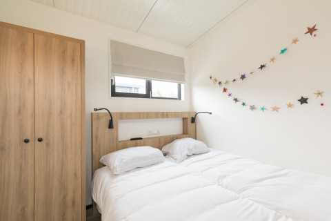 Lichte slaapkamer met tweepersoonsbed, houten kast en feestelijke sterrenslinger in Sea Lodges Ameland 2, Nederland.