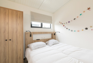 Lichte slaapkamer met tweepersoonsbed, houten kast en feestelijke sterrenslinger in Sea Lodges Ameland 2, Nederland.