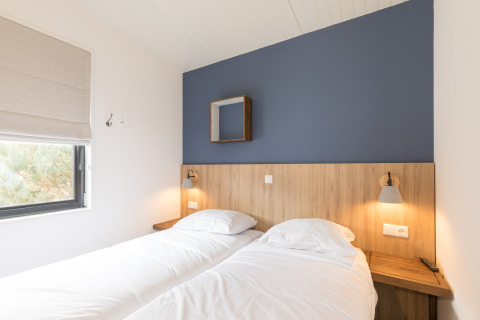 Moderne slaapkamer met twee aparte bedden en blauwe muur in Sea Lodges Ameland, Nederland.
