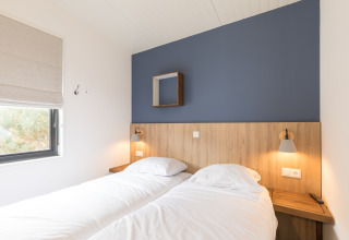 Moderne slaapkamer met twee aparte bedden en blauwe muur in Sea Lodges Ameland, Nederland.