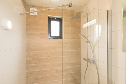 Moderne douche met glazen wand, regendouche en houtlook tegels in Sea Lodges ‘Ameland 2’, Nederland.