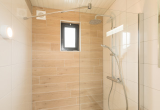 Moderne douche met glazen wand, regendouche en houtlook tegels in Sea Lodges ‘Ameland 2’, Nederland.