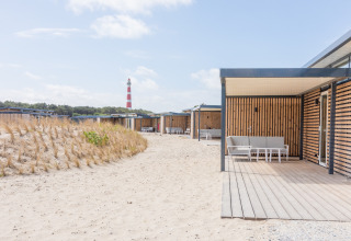 Moderne strandhuisjes met houten panelen en terras, Ameland, Nederland, met vuurtoren op de achtergrond.