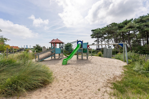 Speeltuin met zand en glijbaan aan Sea Lodges Ameland 2 in Nederland, omgeven door natuur en bomen