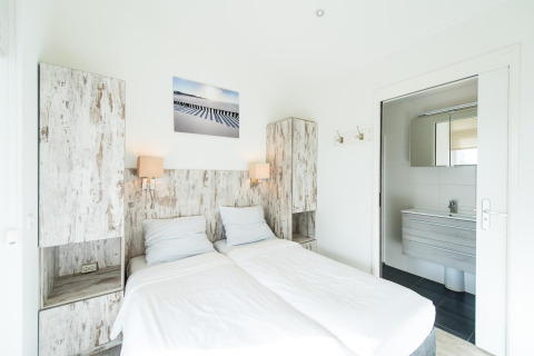 Bright bedroom with two single beds, rustic wood cabinets and en suite bathroom at Boomhiemke, Netherlands.