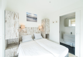 Helles Schlafzimmer mit zwei Einzelbetten, Holzmöbeln und Bad im Ferienpark Boomhiemke, Niederlande.